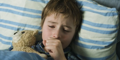 Sick boy in bed coughing with Teddy-bear